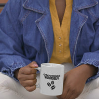 Person wearing a denim jacket holding a coffee mug with 'Espresso Yourself' text and coffee bean design.