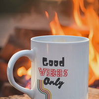 Good Vibes Only mug with colorful text beside a campfire, promoting positive energy and motivation.