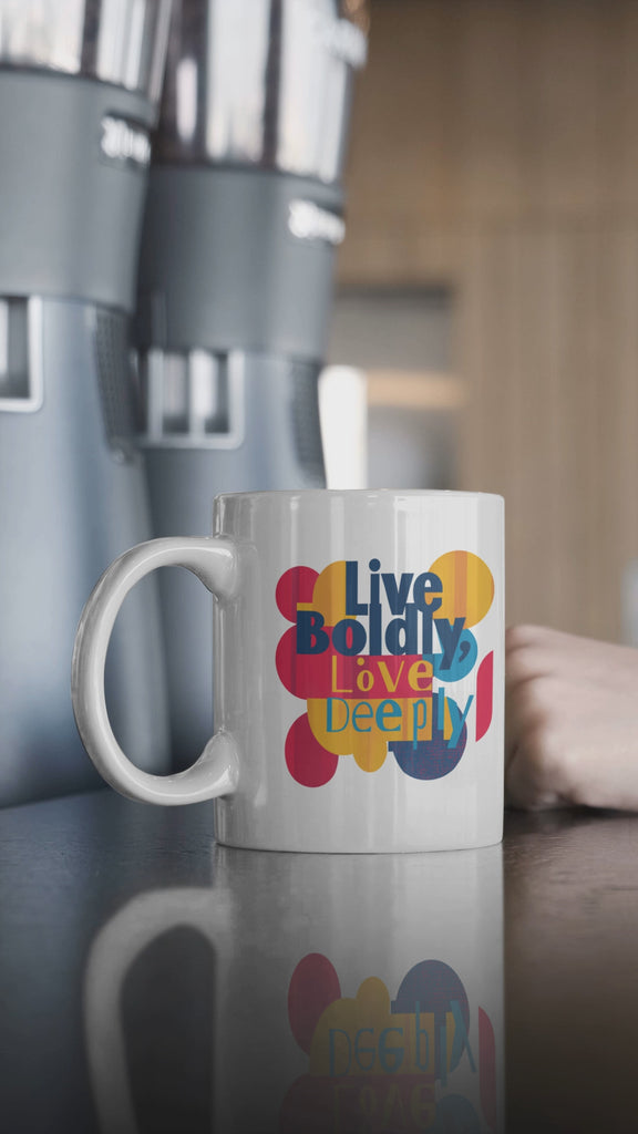 Stylish 11 oz mug with 'Live Boldly, Love Deeply' in vibrant colors and curvy shapes on a kitchen counter.