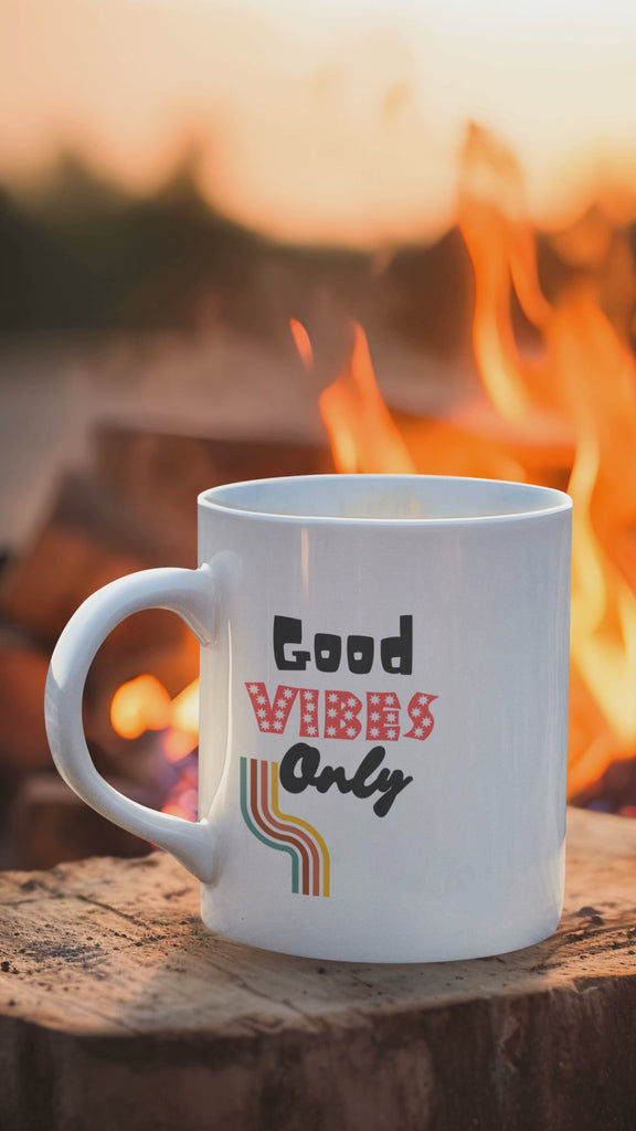 Good Vibes Only mug with colorful text beside a campfire, promoting positive energy and motivation.